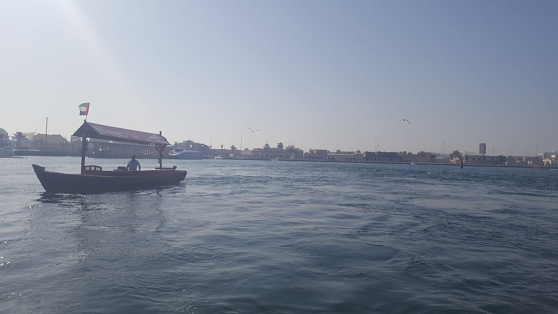 A wooden abra water taxi crossing Dubai Creek, with low buildings on the far bank