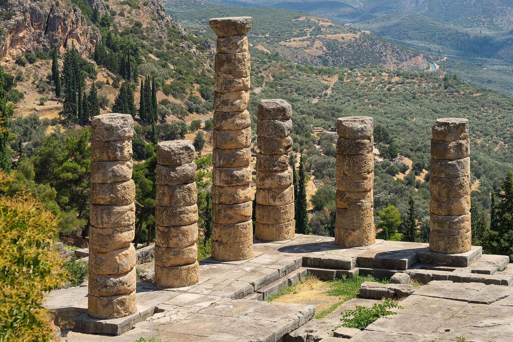 Six weathered columns of the Temple of Apollo at Delphi above olive groves in the valley of Mount Parnassus