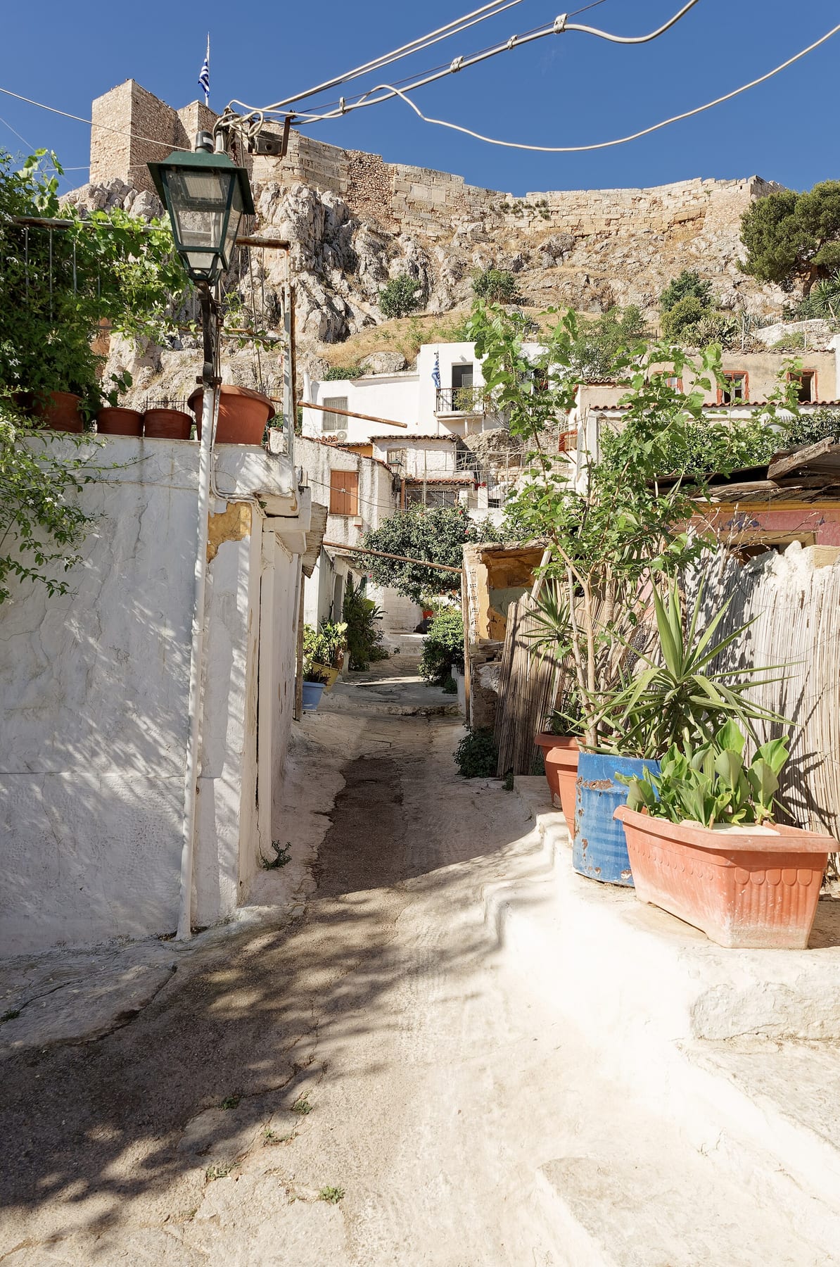 A whitewashed lane in Anafiotika with potted plants, below the rock and walls of the Acropolis