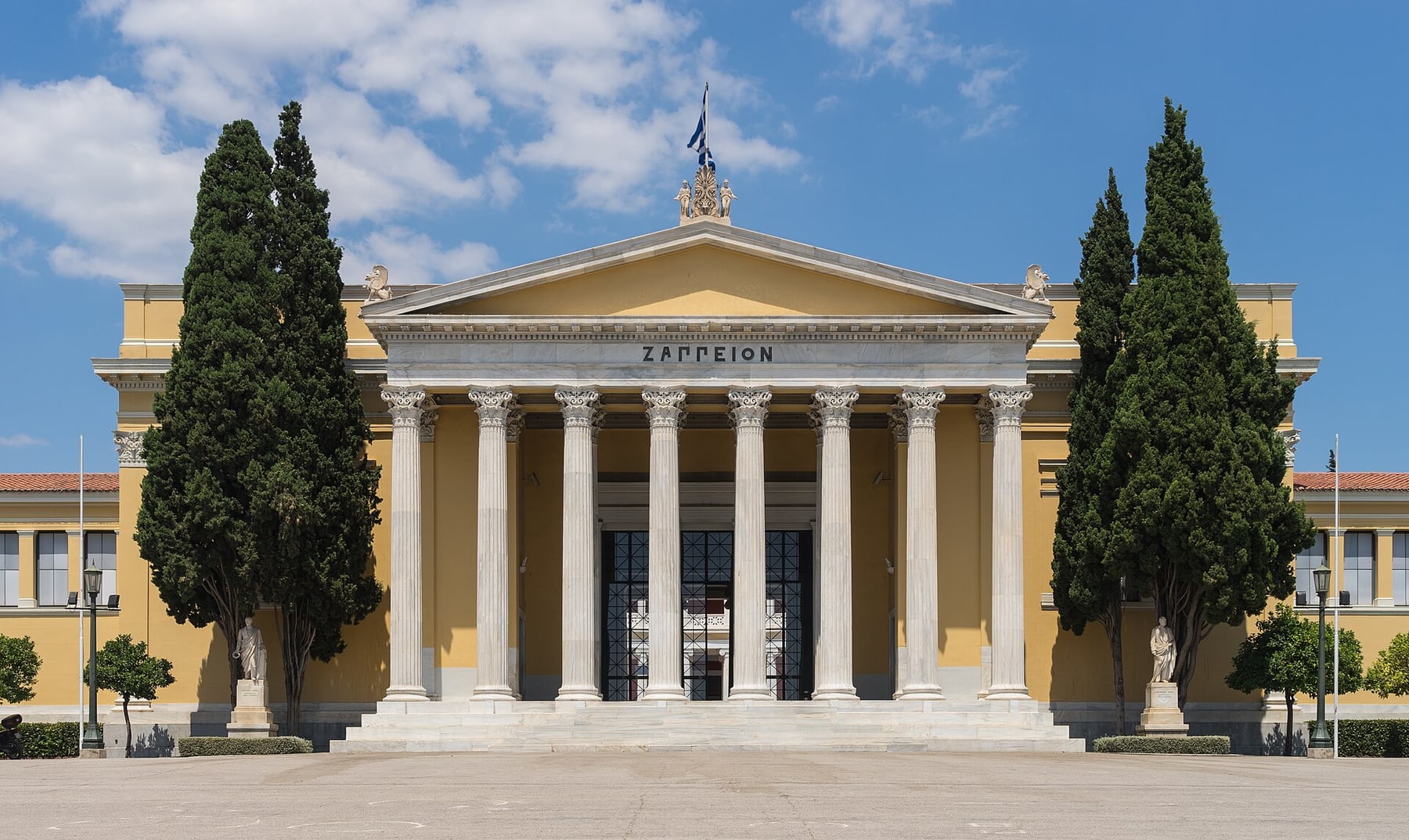 The columned front of the Zappeion in Athens, a yellow neoclassical hall with a white marble portico framed by two cypress trees