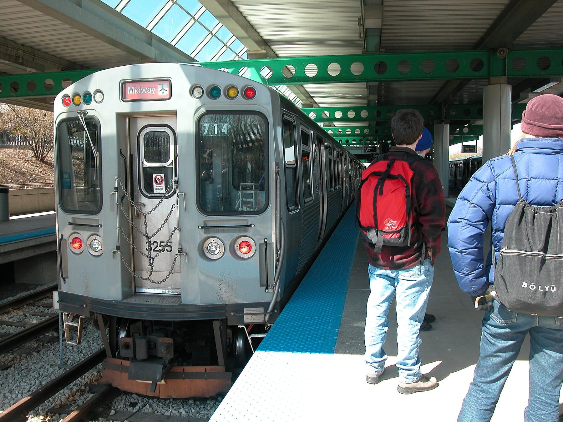 A CTA Orange Line train signed Midway standing at the Midway station platform, with passengers waiting beside it