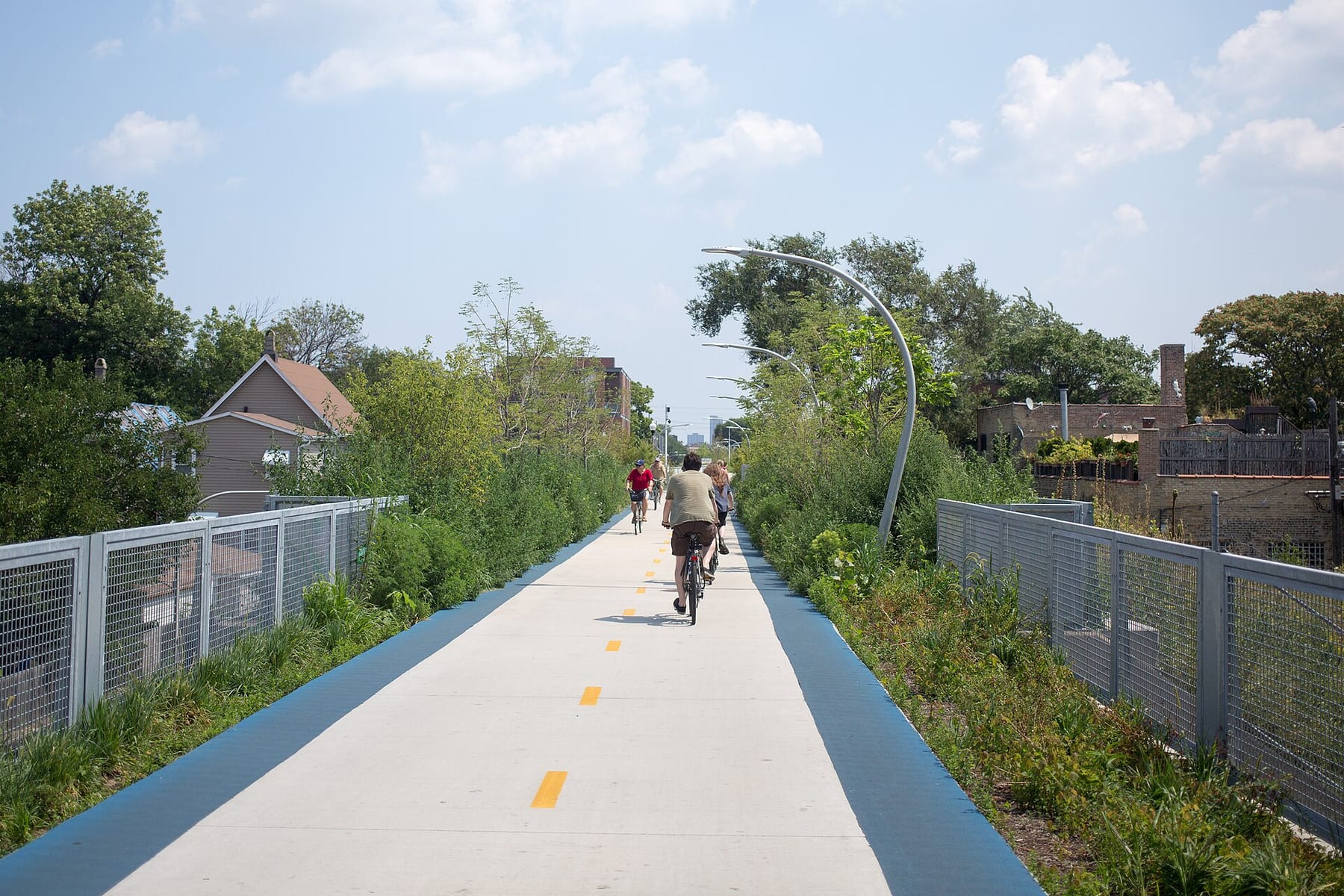 Cyclists riding along the elevated Bloomingdale Trail, the 606, between rows of low buildings on Chicago’s northwest side