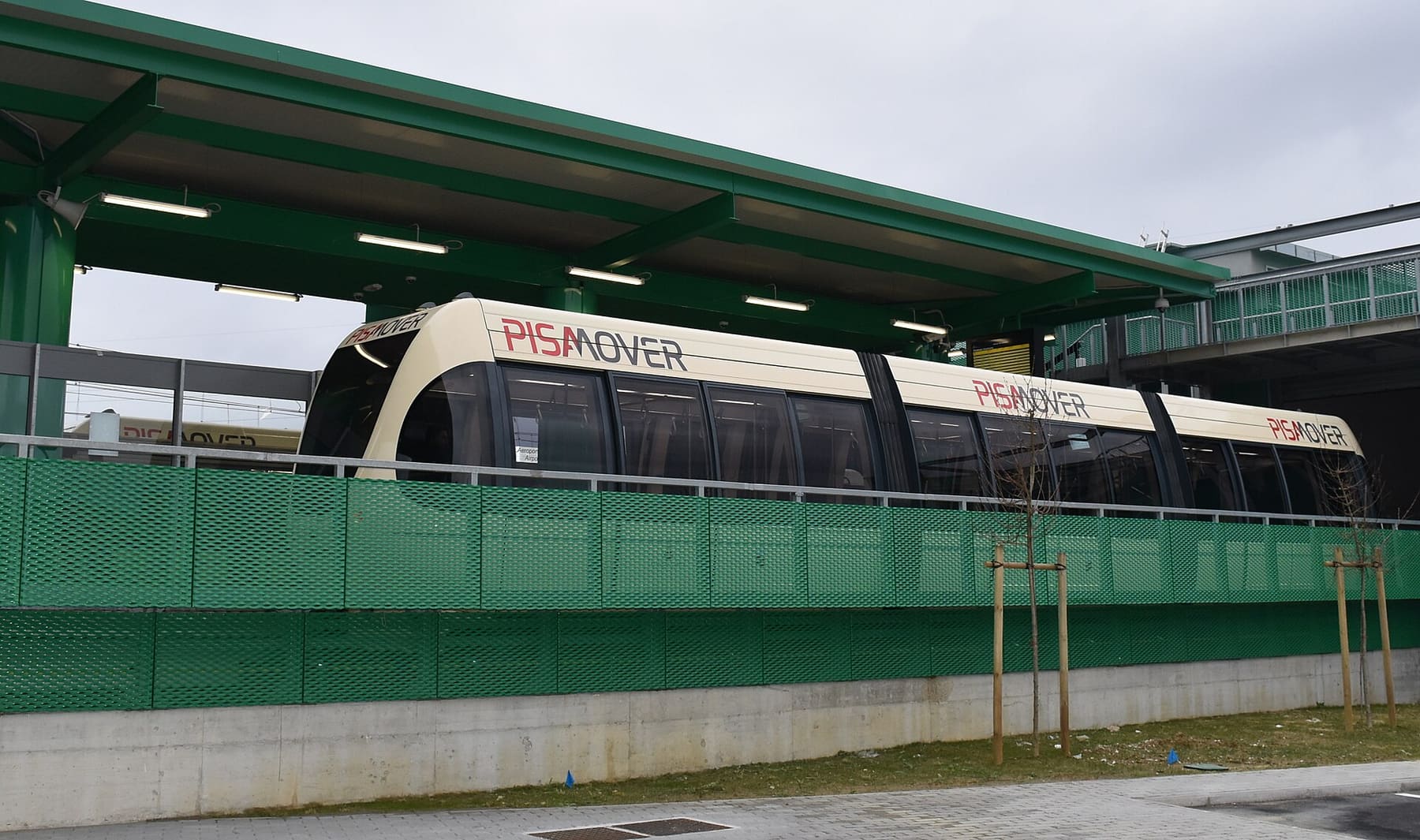 A PisaMover shuttle train standing at its stop beside a green canopy