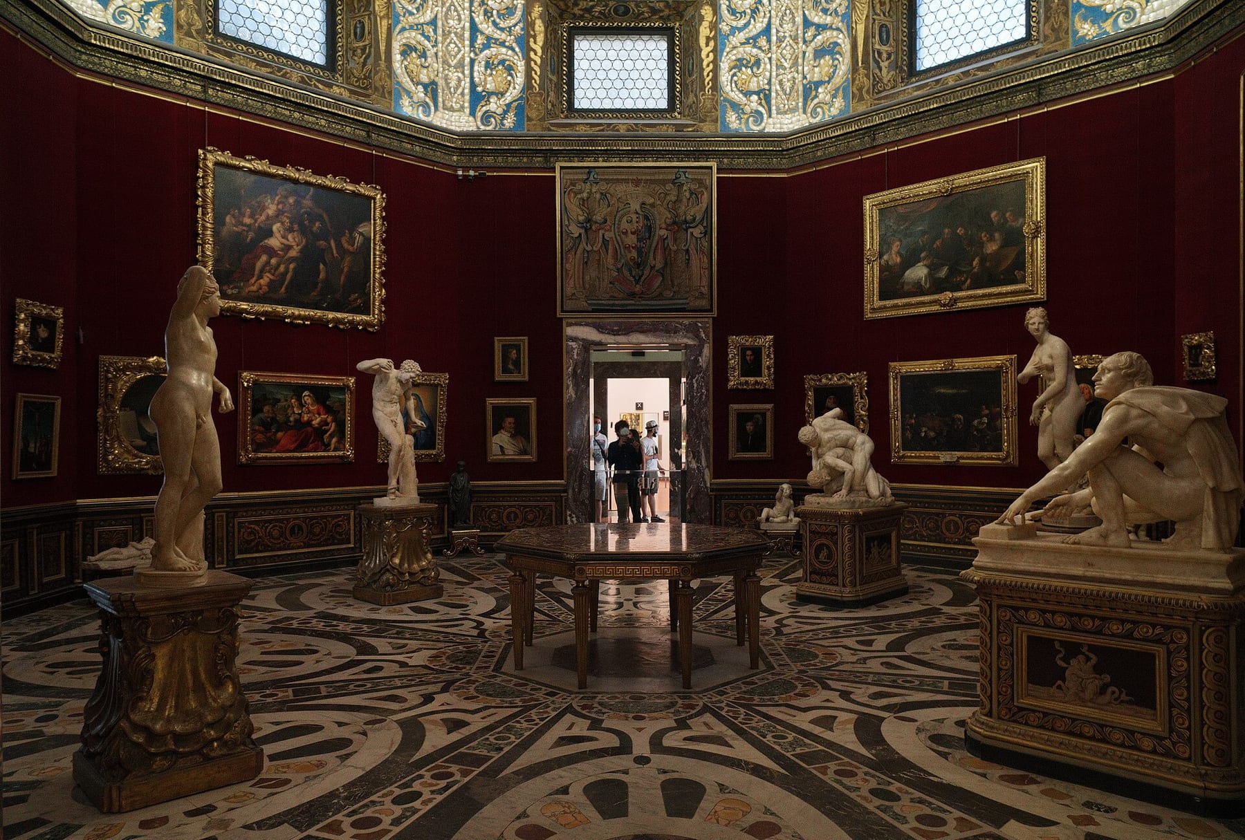 The red-walled Tribuna room inside the Uffizi Gallery in Florence, with marble statues and framed paintings, on the guided visit priced here