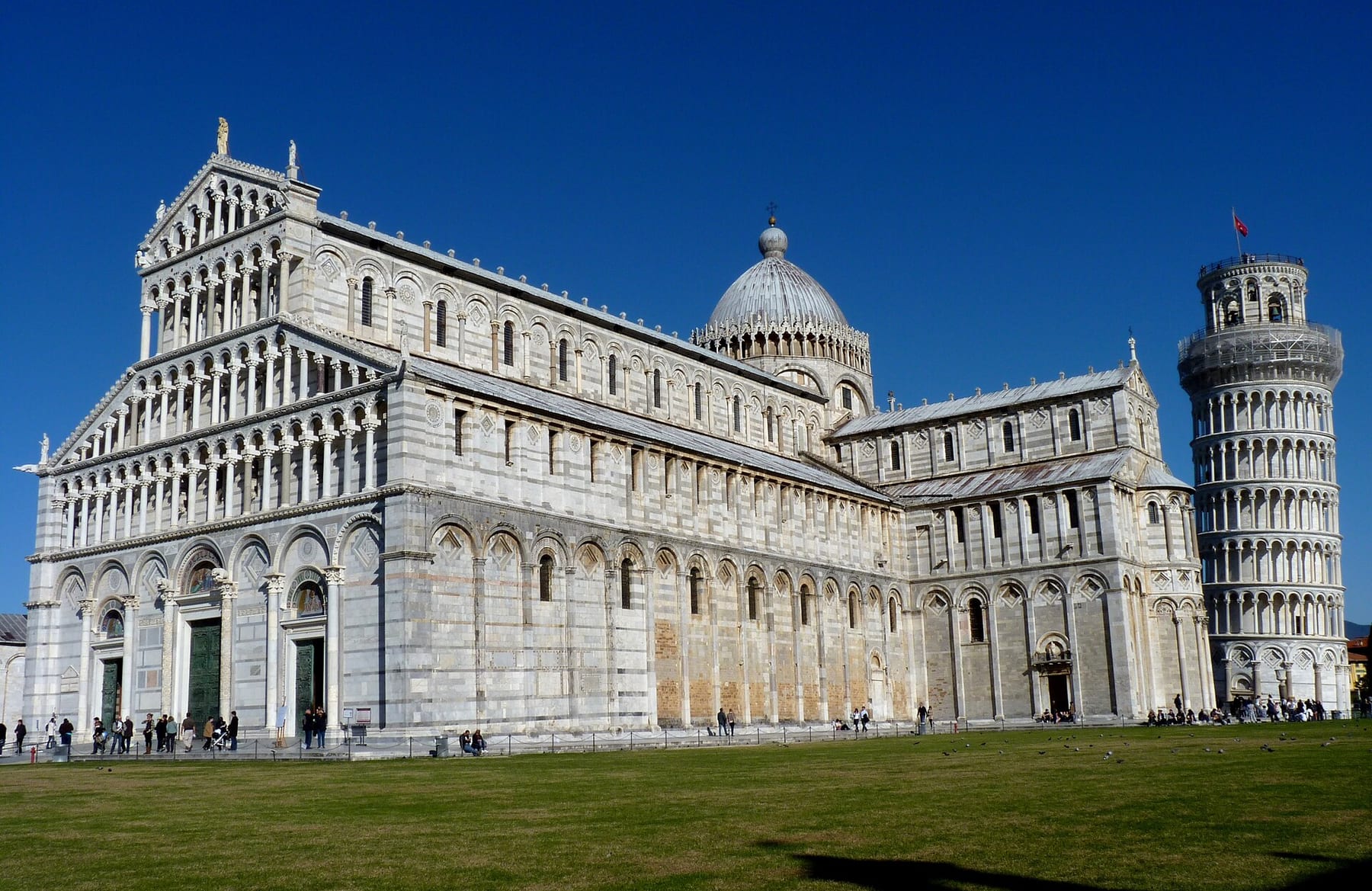 The white-marble Pisa Cathedral and the Leaning Tower beside it on the lawn of Piazza dei Miracoli