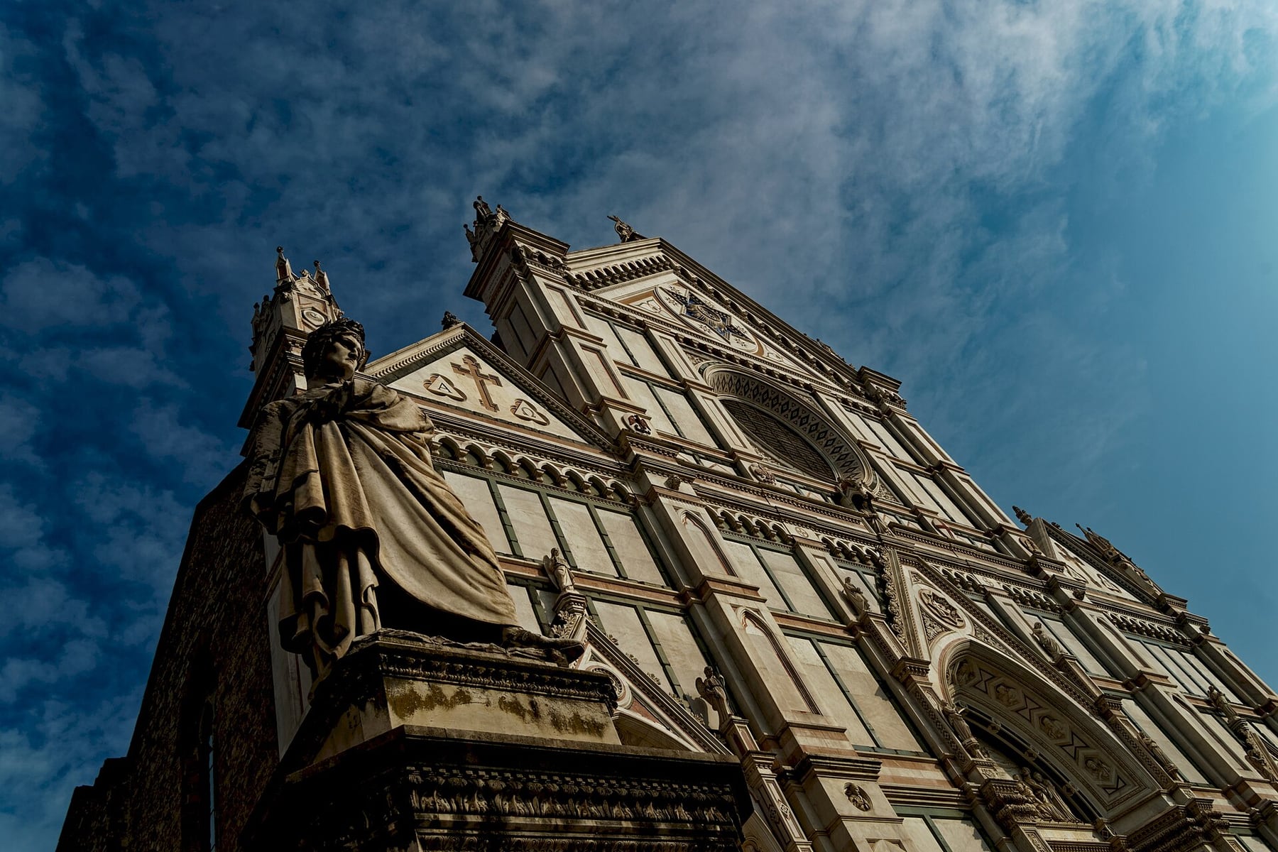 The white, green and pink marble facade of the Basilica of Santa Croce in Florence, with the statue of Dante on its plinth in the foreground