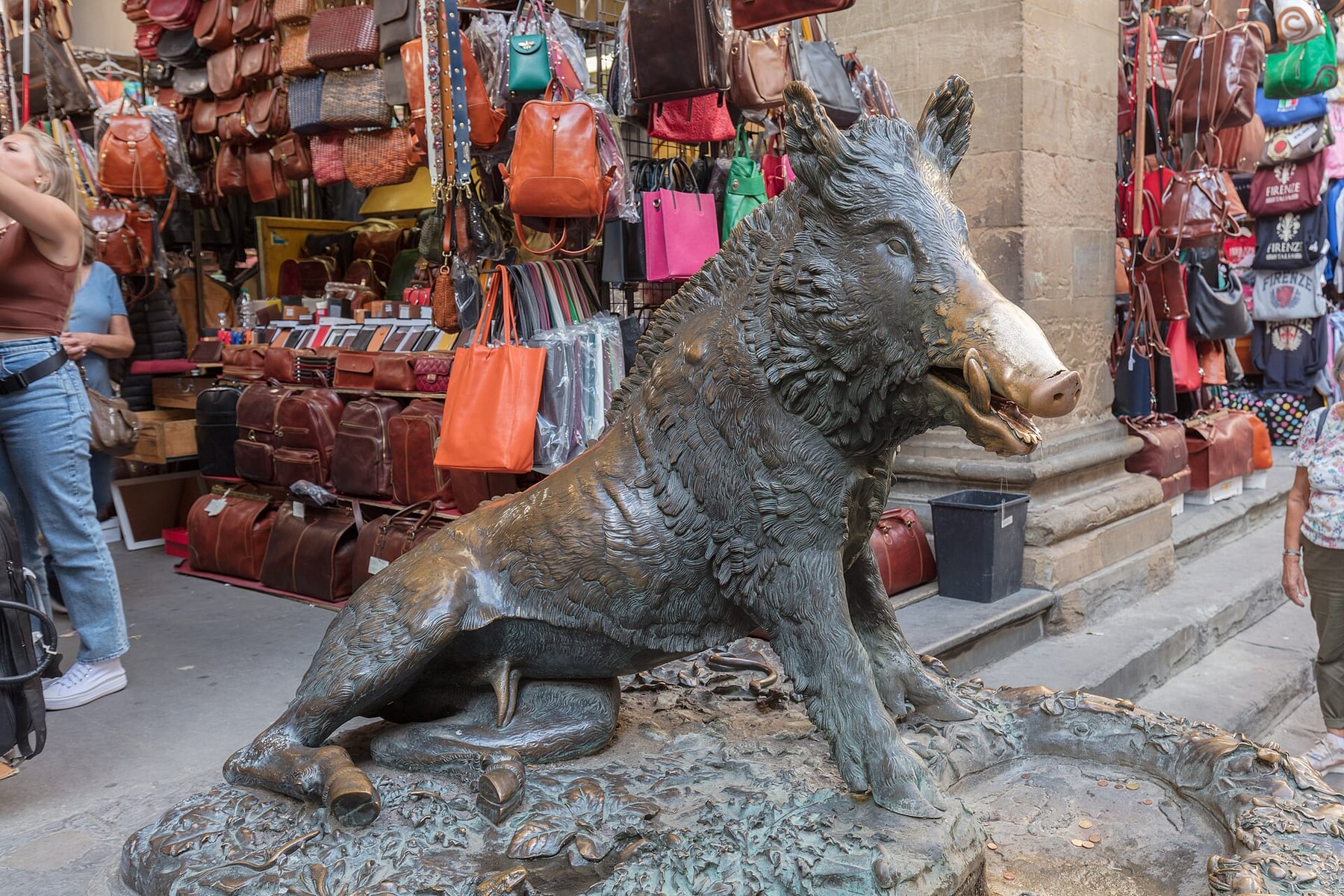 The bronze Porcellino boar fountain in the Loggia del Mercato Nuovo in Florence, with leather bags on the market stalls behind it