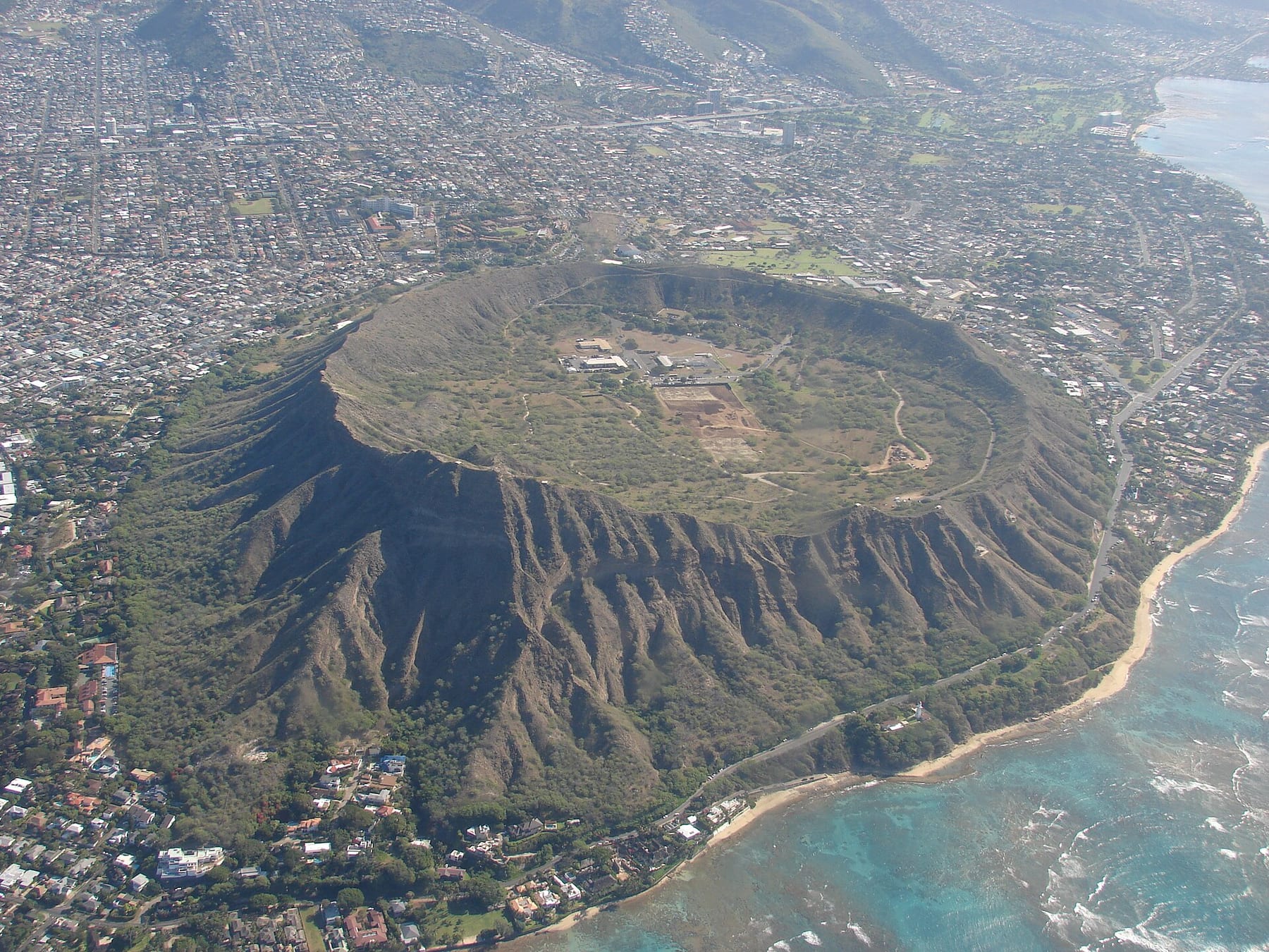 Aerial view of the Diamond Head crater from the air, with its ridge, the crater floor and the surf along the coast