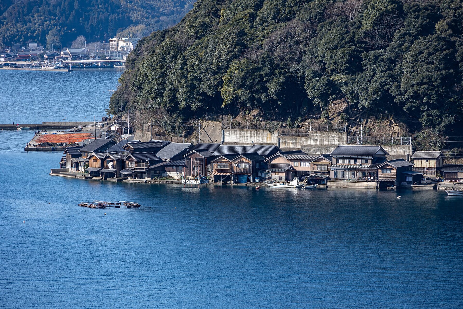 Wooden funaya boathouses along the water’s edge at Ine, with forested hills behind