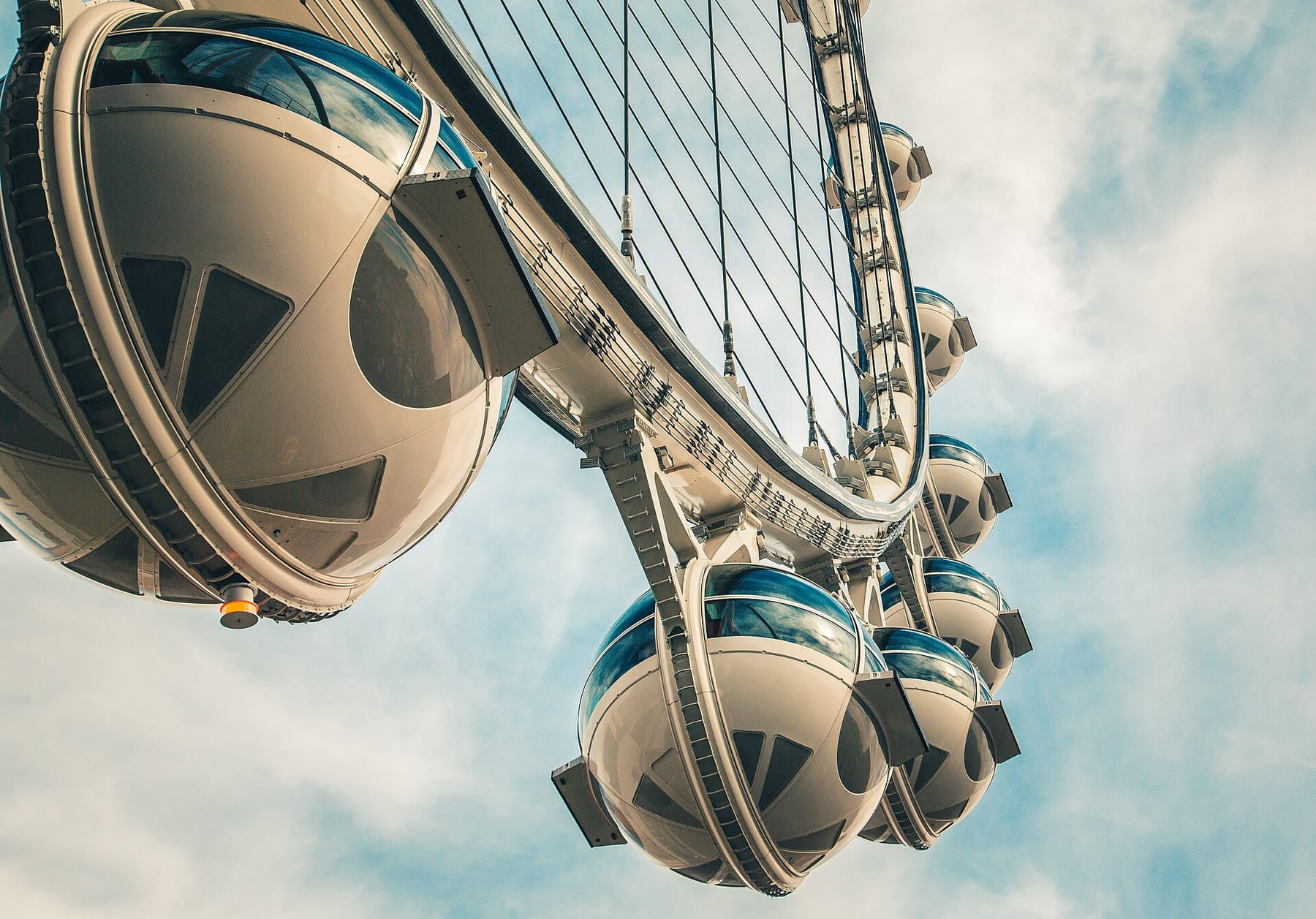 Glass-topped cabins of the High Roller observation wheel hanging from its rim against a cloudy sky, the wheel on this three-ticket route