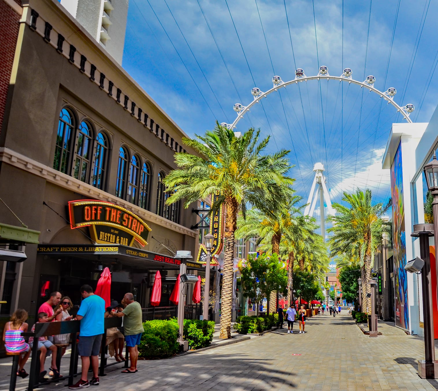 The LINQ Promenade on a sunny day, lined with palm trees and leading toward the High Roller wheel