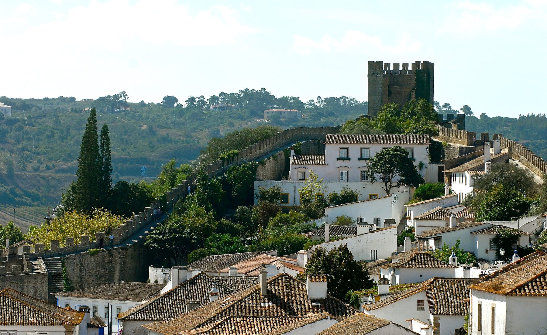 The square tower of Óbidos castle above white houses with terracotta roofs and the town walls