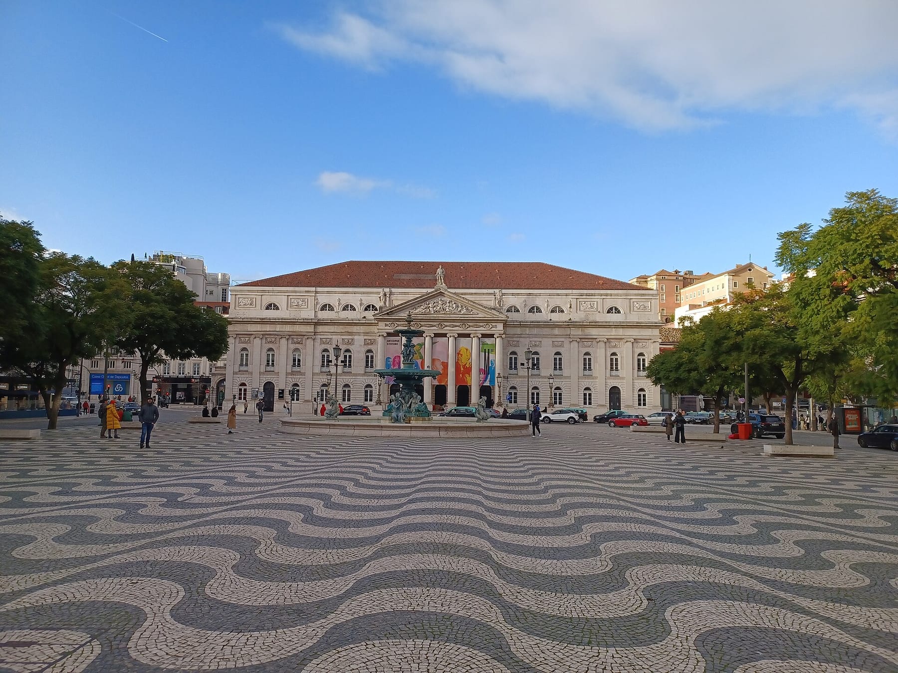 The wave-patterned black-and-white pavement of Rossio Square in Lisbon, with its fountain and the Dona Maria II National Theatre behind