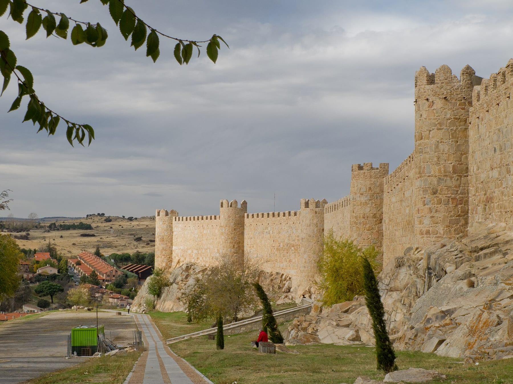 Battlemented towers of Ávila’s medieval city walls rising above a path and a rocky slope