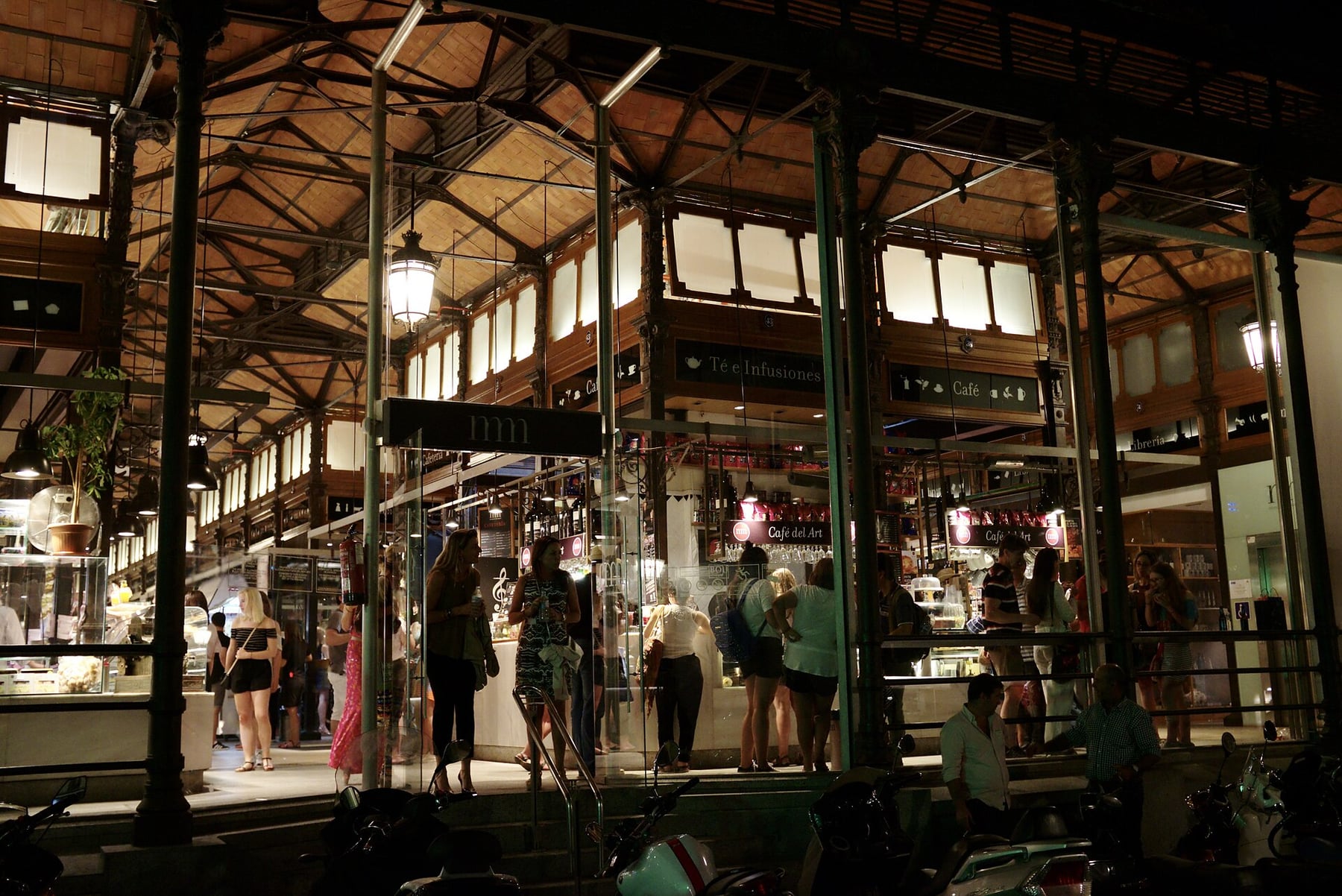 The iron-and-glass hall of Mercado de San Miguel lit at night, with visitors at its stalls