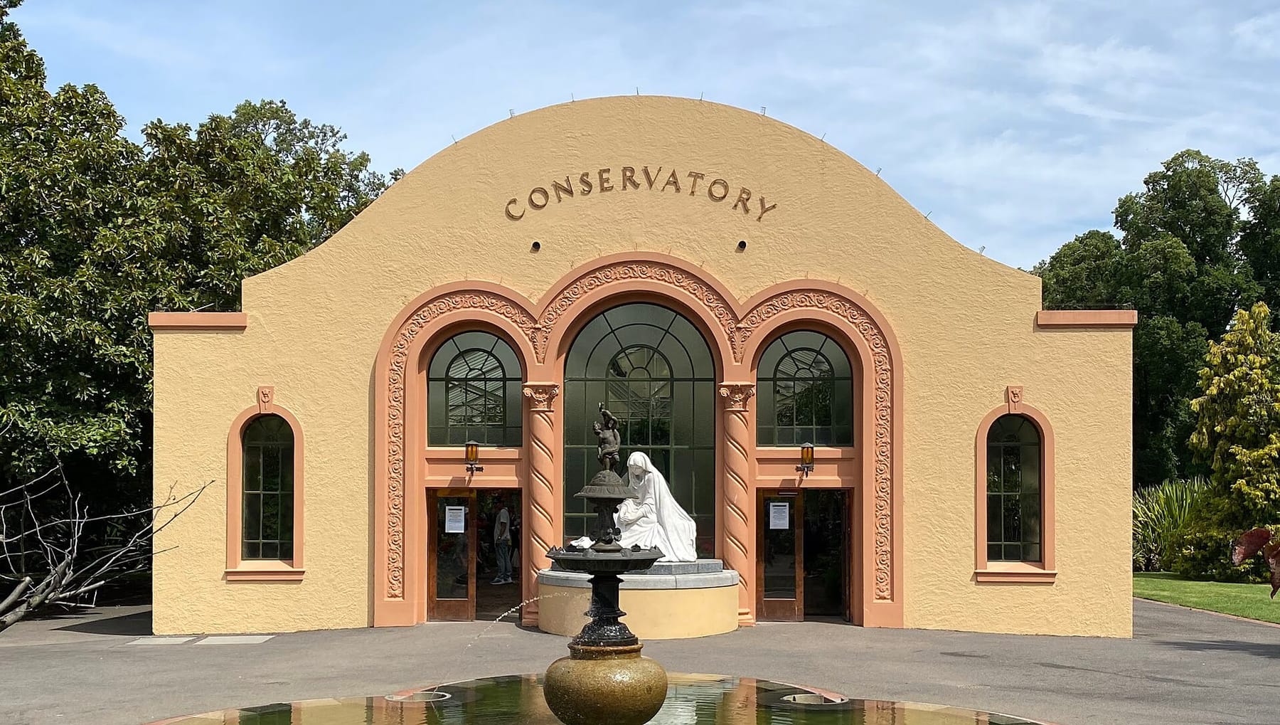 The Spanish mission-style Conservatory in Fitzroy Gardens, with a fountain and a white statue at its entrance
