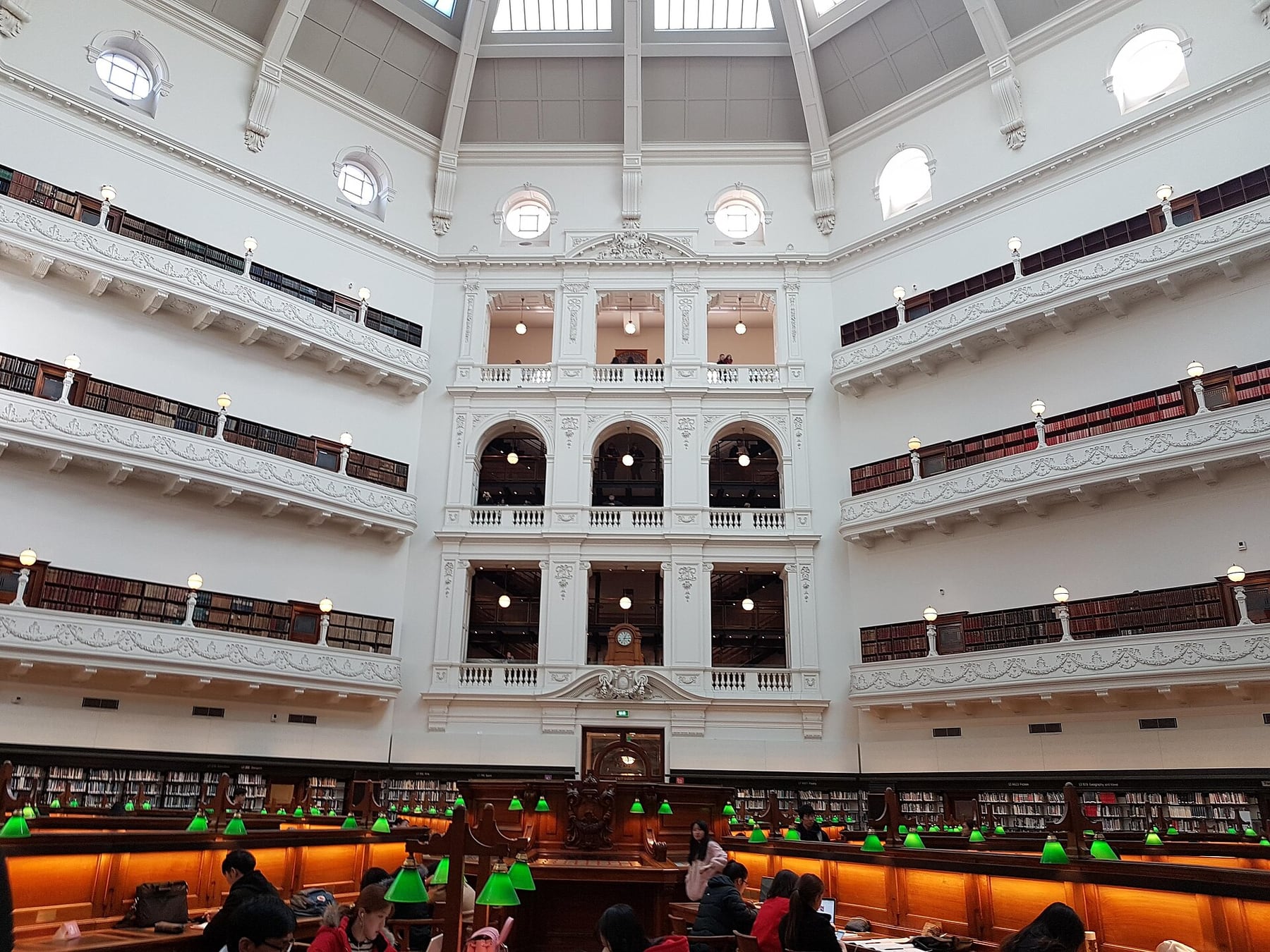 The La Trobe Reading Room at State Library Victoria, with tiers of white balconies above rows of desks with green lamps