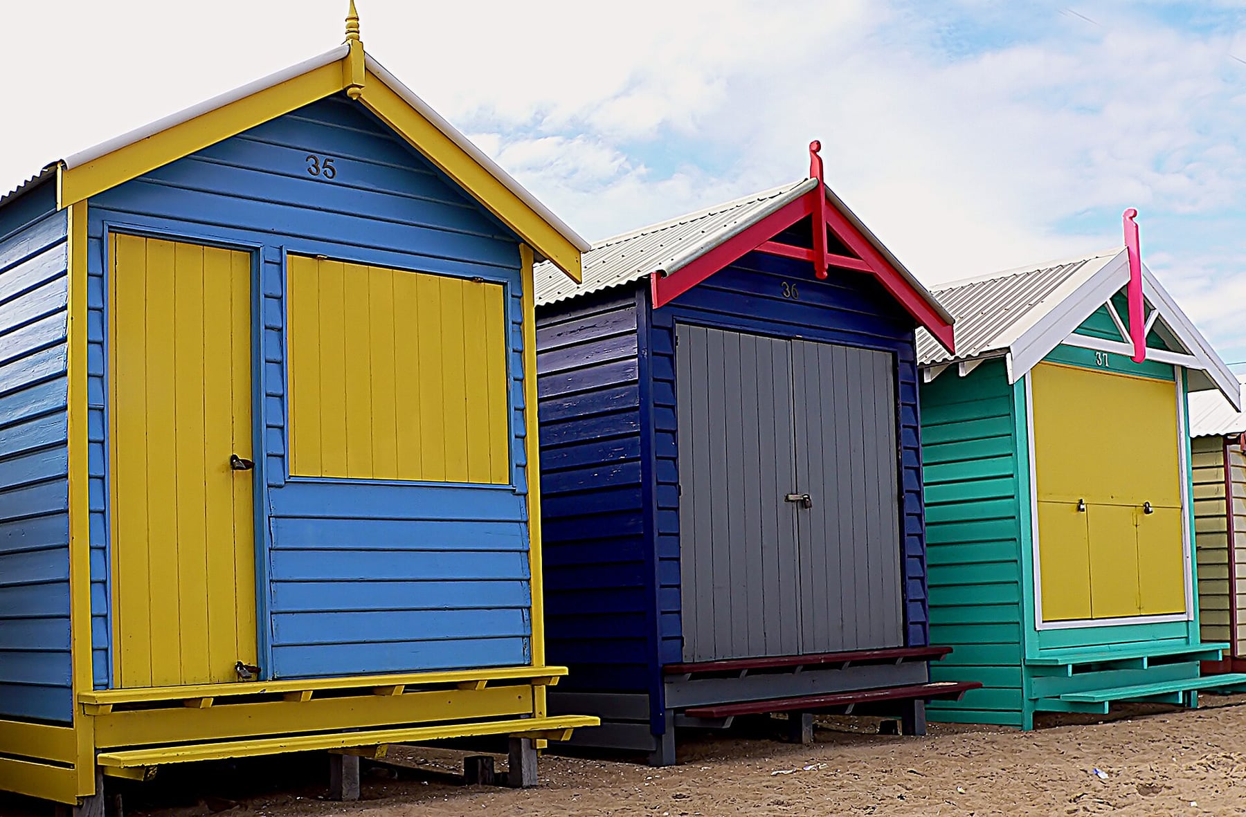 Three brightly painted timber bathing boxes on the sand at Dendy Street Beach, Brighton, Melbourne