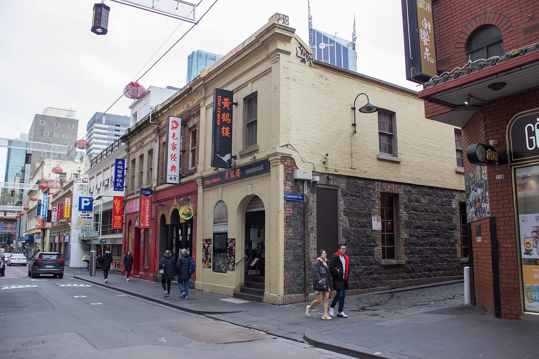 A heritage corner building of bluestone and yellow brick on Little Bourke Street in Chinatown, with lanterns strung across the street